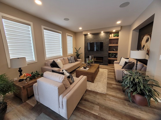 living room with three large windows white chairs and a tv mounted over an electric fire place